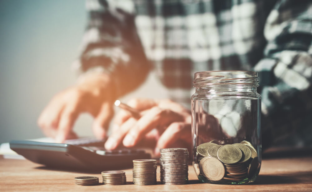 Sloik z monetami na pierwszym planie, na drugim - mężczyzn z kalkulatorem. Habza Finanse to kredyty nie tylko na umowę o pracę